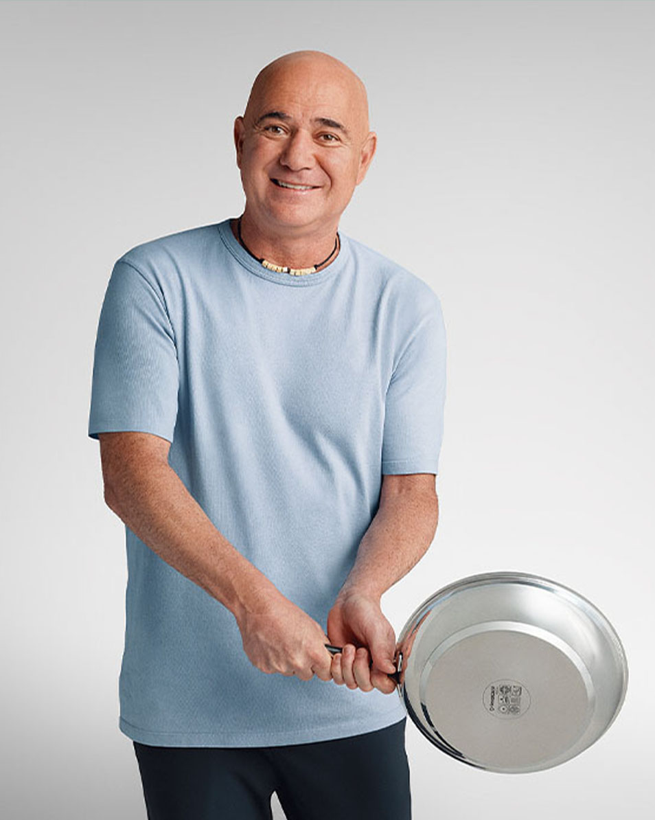 Smiling bald man in a light blue T-shirt, holding a stainless steel frying pan.