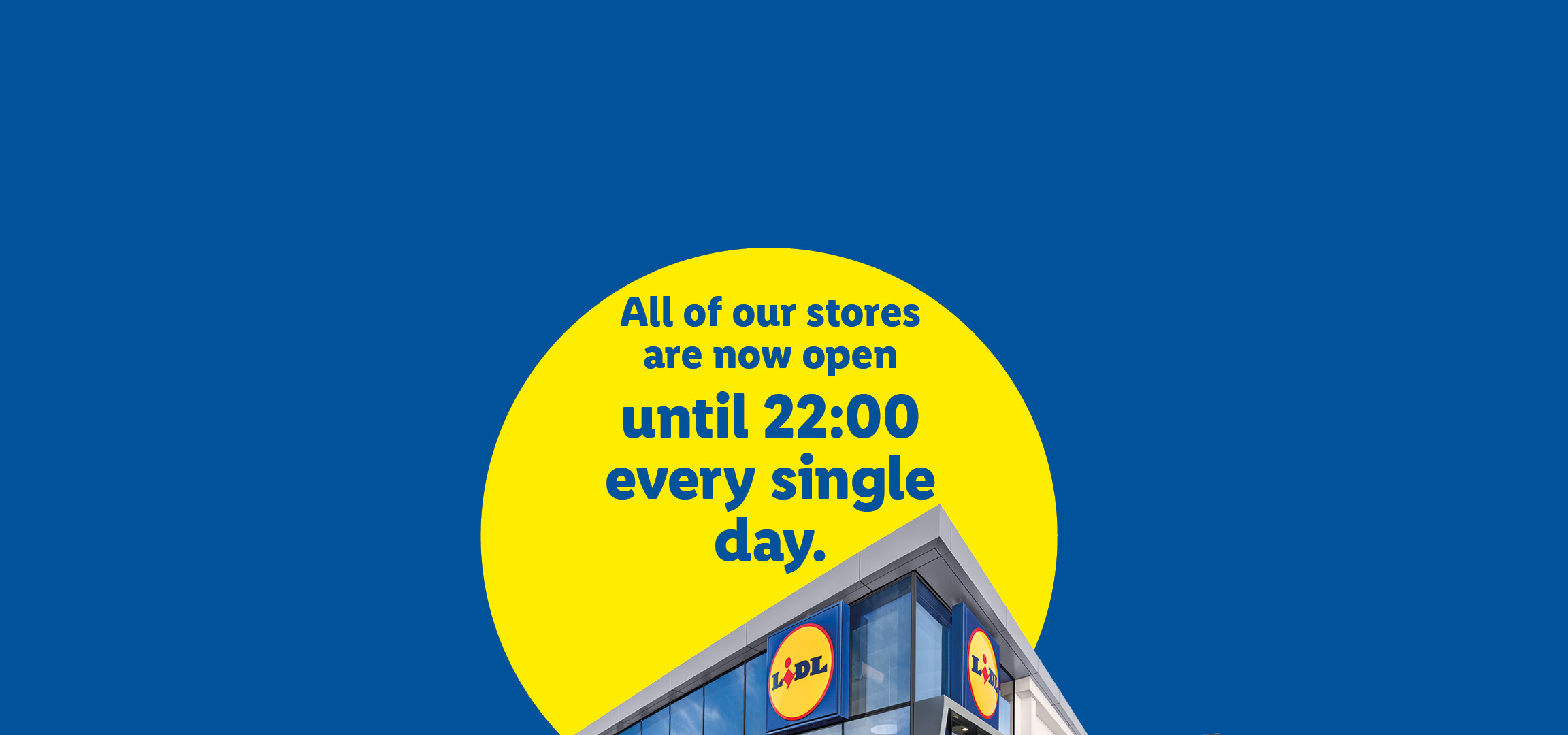 A modern supermarket building with a yellow circle containing text: 'All of our stores are now open until 22:00 every single day.'