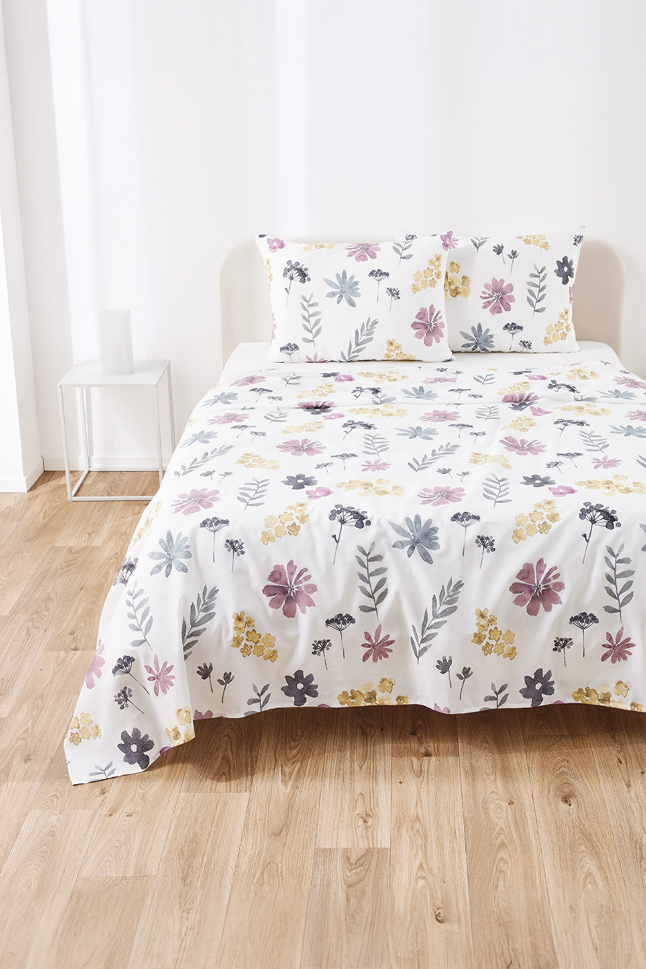 White bedding set with colorful floral patterns on a bed in a bright room.