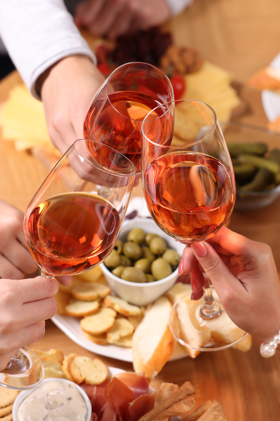 Three people toasting with glasses of rosé wine, surrounded by a platter of snacks.
