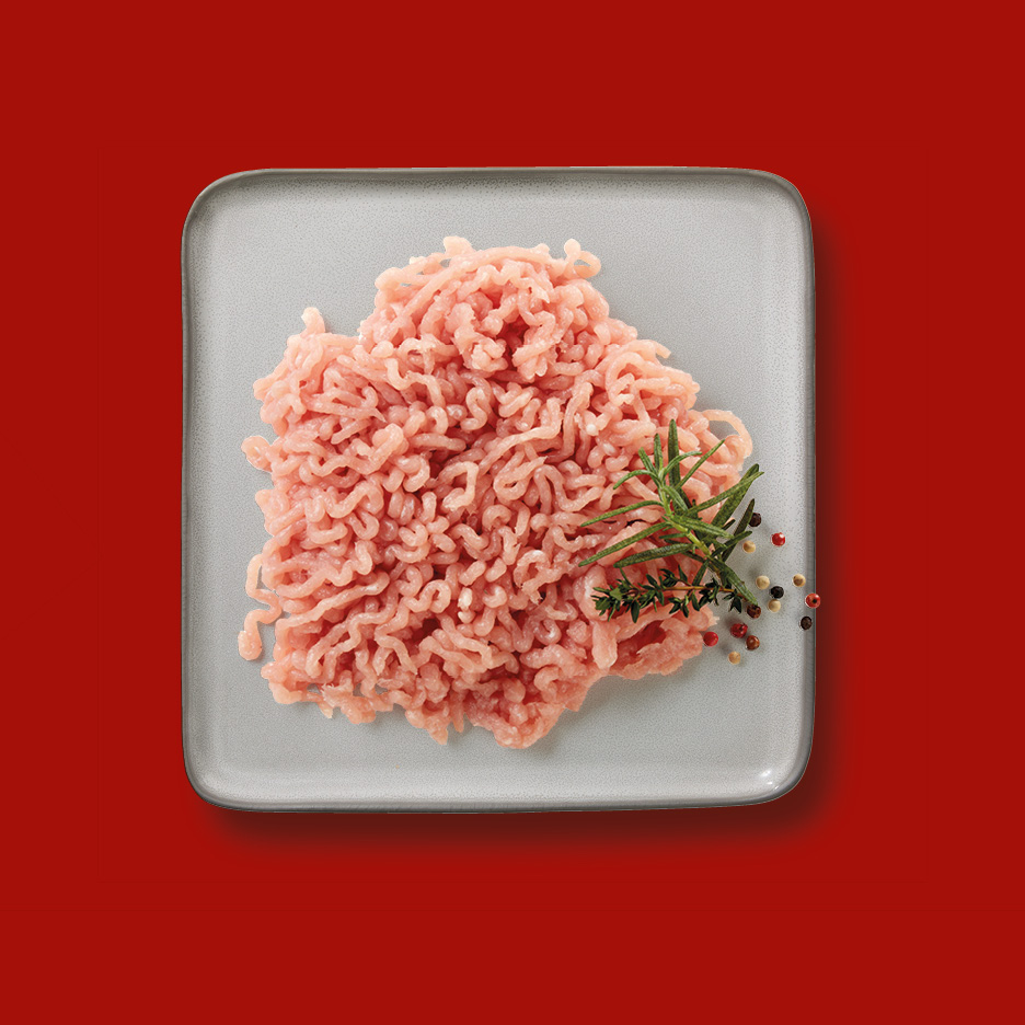 Minced turkey meat on a grey plate with rosemary and peppercorns on a red background.