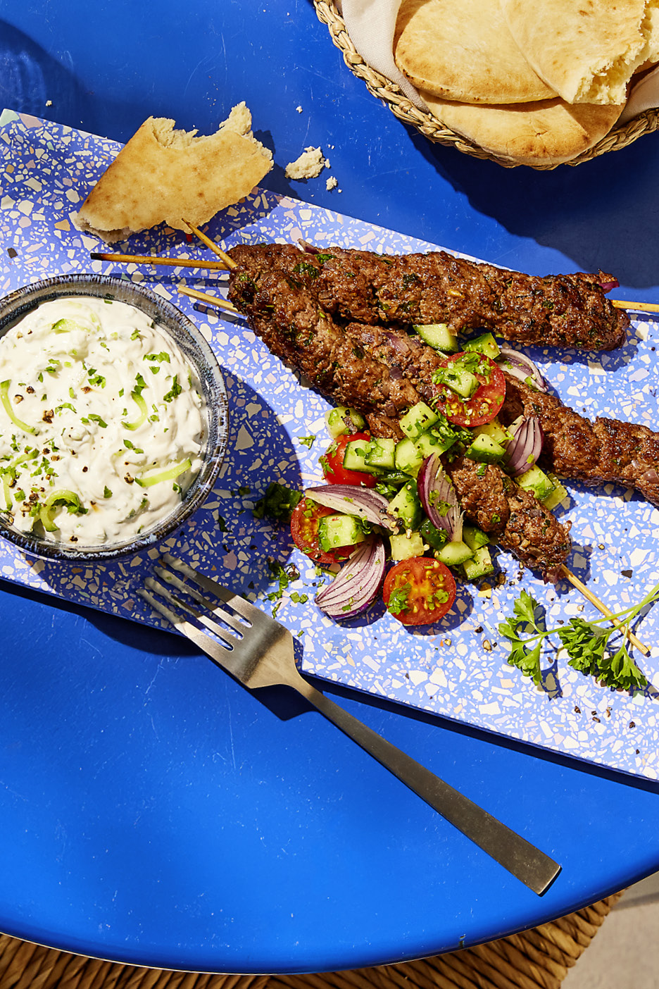 Grilled lamb kofta skewers with tzatziki, tomato and cucumber salad, and pita bread.