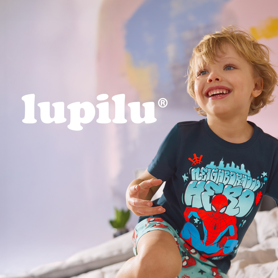 Smiling boy in a dark blue t-shirt and light blue shorts with a superhero print.