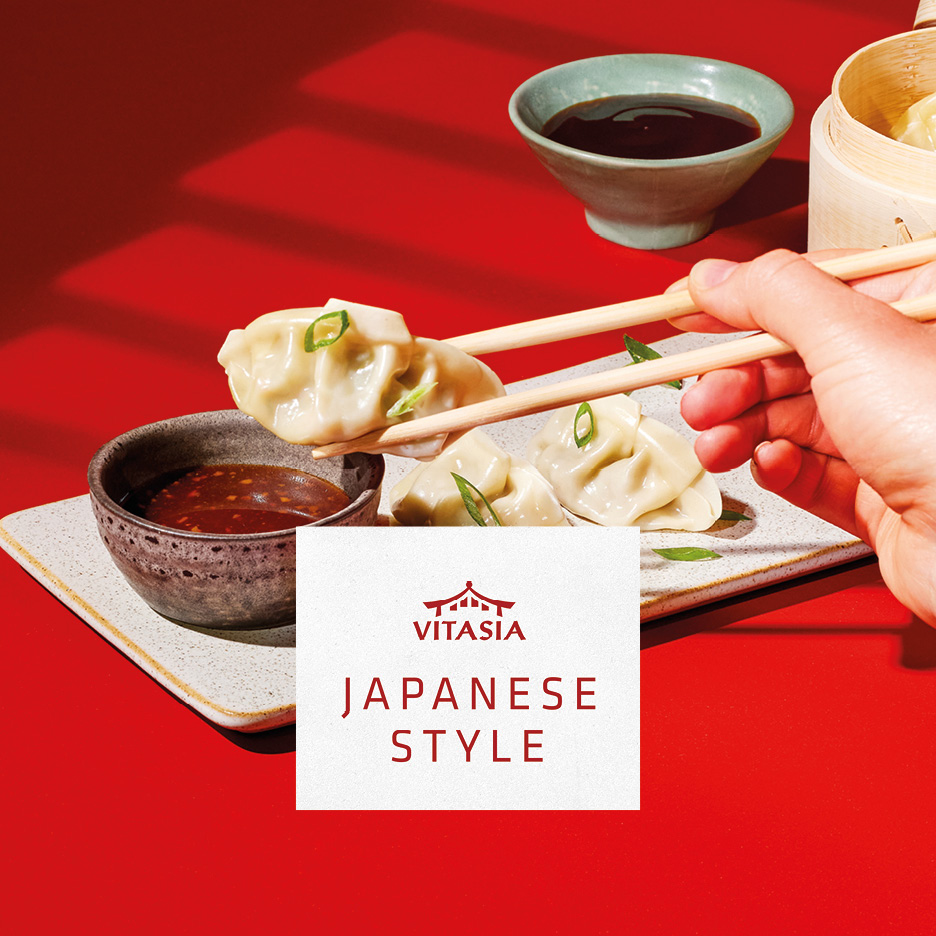 Japanese style dumplings with dipping sauces, held by chopsticks on a red background.
