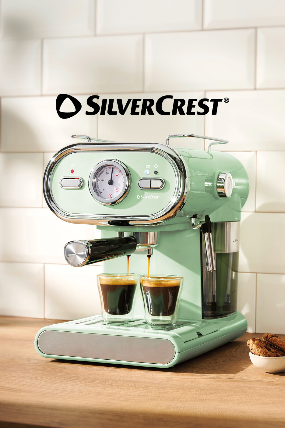 Mint green espresso machine brewing coffee into two glasses on a wooden counter.