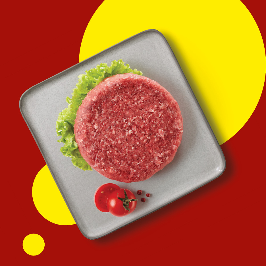 Raw beef burger patty with lettuce and tomato slices on a grey plate.