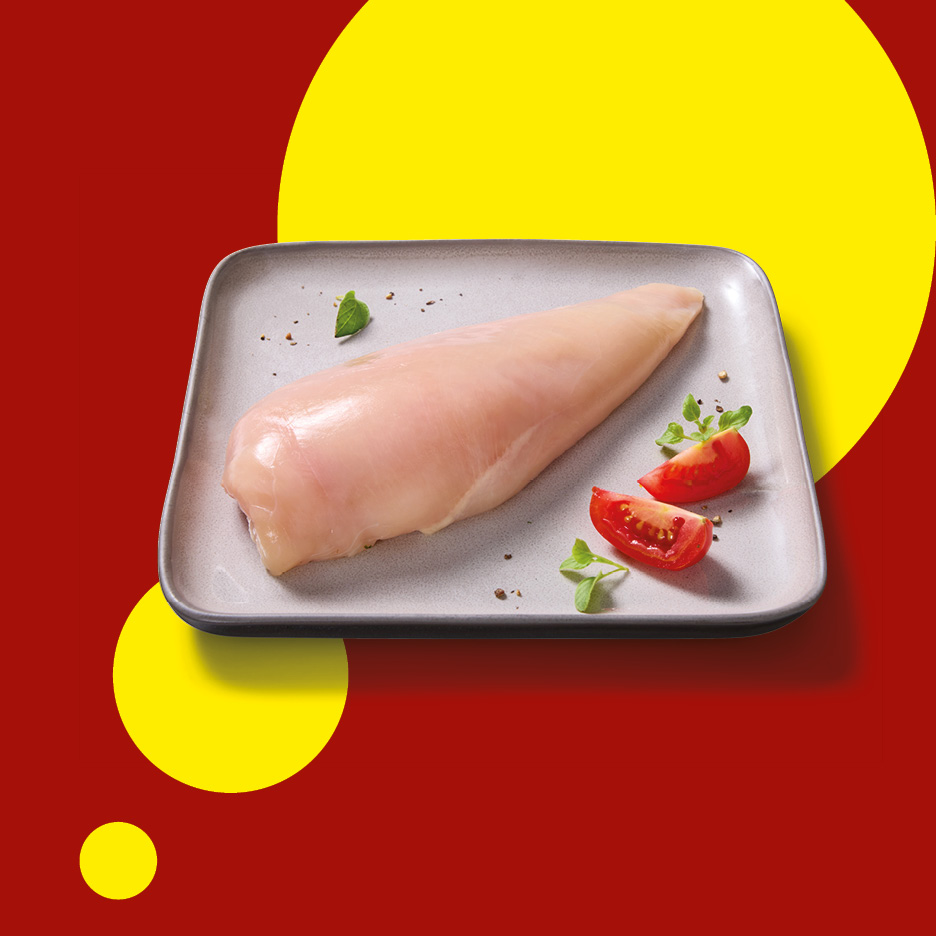 Raw chicken breast on a plate with tomato and herbs, on a red and yellow background.