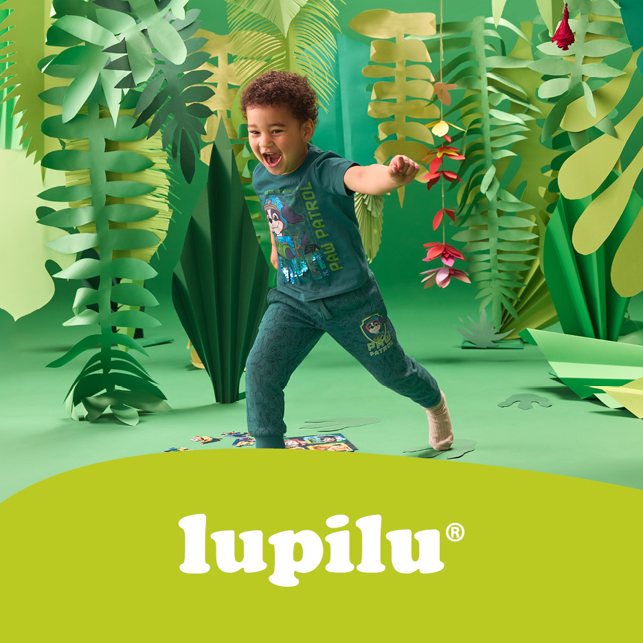 A happy child in a green Paw Patrol outfit, playing in a jungle-themed setting.