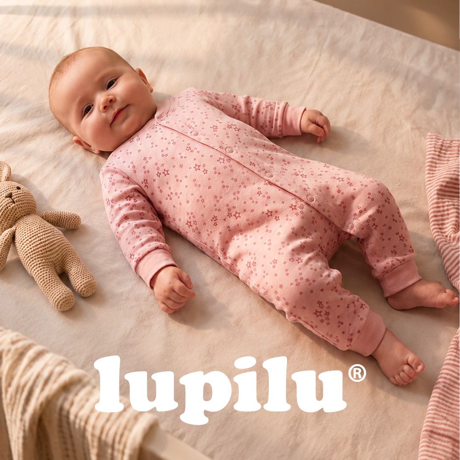 Baby in pink star-patterned sleepsuit, lying on a blanket with a knitted bunny toy.