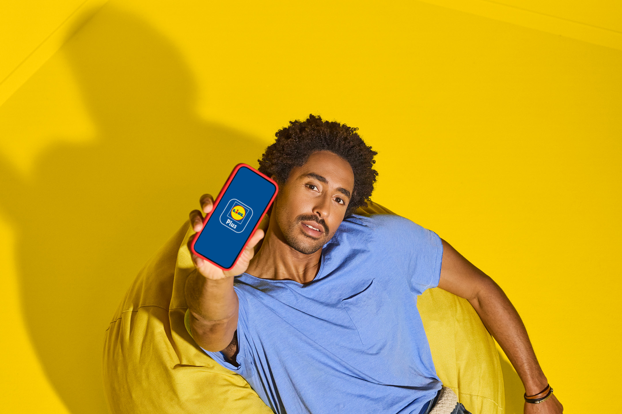 Man holding a smartphone with a loyalty program app on a yellow background.